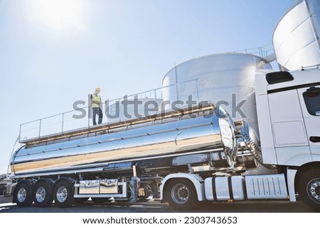 Worker on platform above stainless steel milk tanker