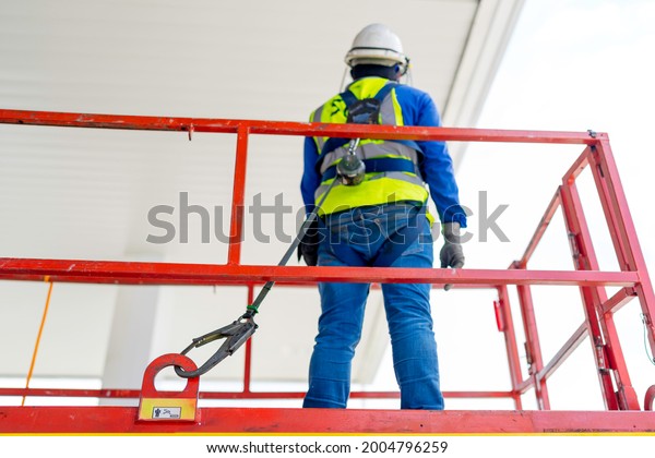 Worker on a Scissor Lift\
Platform preprinting for working at site focus on full harness\
safety belt.