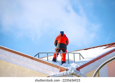 Worker on snowy roof preparing remove snow and ice, industrial alpinist at winter work. Worker stand on building roof, ready remove snow and break ice and icicles on roof top. Risky work at height