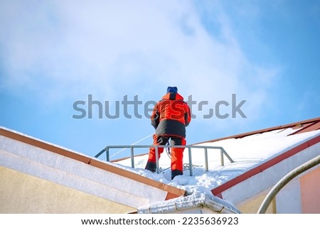 Worker on snowy roof preparing remove snow and ice, industrial alpinist at winter work. Worker stand on building roof, ready remove snow and break ice and icicles on roof top. Risky work at height