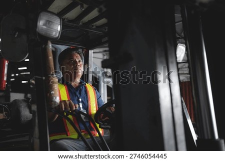 Worker operates forklift with focused expression. Dark interior contrasts bright safety vest. Hands grip controls, eyes forward, ready to act. Industrial setting suggests heavy-duty work