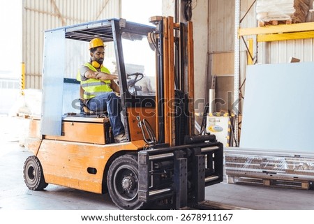 Worker operates a forklift inside a warehouse, unloading materials. He wears a hardhat and safety vest, displaying safe practices. The industrial setting reflects logistics and goods handling 