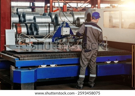 Worker operates mechanical vacuum lifter in metalworking factory.