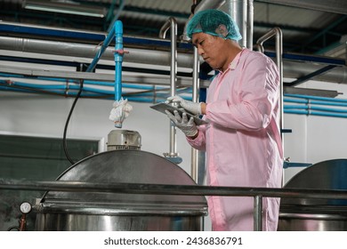 Worker operates a tablet overseeing beverage production while an engineer supervises soda water filling. Emphasizing quality control ensures top-tier standards in bottle manufacturing. - Powered by Shutterstock