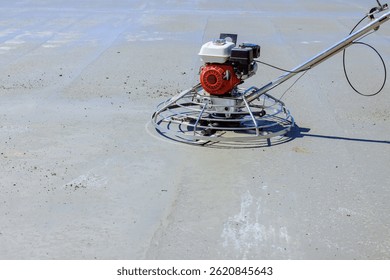 Worker operates trowel machine to level freshly poured concrete in open construction area, ensuring flawless finish.