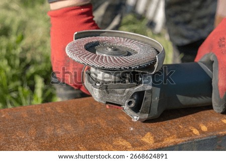 A worker operating an angle grinder with an abrasive disc on a rusted metal surface outdoors. Precision, craftsmanship, manual labor.