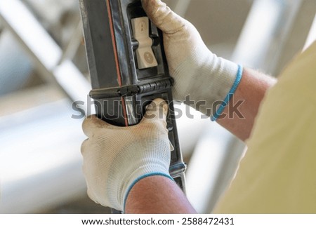 Worker operating a hoist crane control panel with protective gloves in an industrial setting