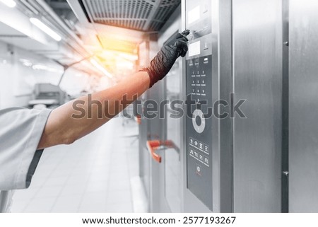 Worker operating oven control panel in modern bakery factory.