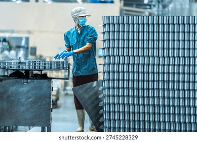 Worker operating a pallet jack to move stacked cans in a food production warehouse Focus on industrial logistics efficiency and organized manufacturing processes.