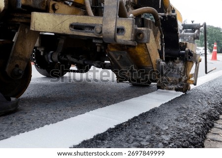 Worker operating road marking machine applying white line on new asphalt pavement. Road maintenance and construction concept, ensuring traffic safety and infrastructure quality.