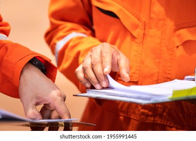 A Worker In Orange Coverall Uniform Is Opening Documents To Make A Discussion On Working Procedure, Safety Audit In Operation Action Photo. Close-up And Selective Focus On Human's Hand.