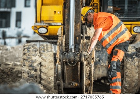 A worker in an orange shirt is using a machine at a construction site. The scene shows dirt and machinery.