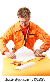 Worker In Orange Work Wear Carefully Folds A Paper Sheet, Isolated On White