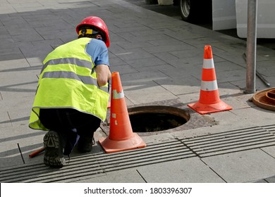 Worker over the open sewer hatch on a street near the traffic cones. Concept of repair of sewage, underground utilities, water supply system, cable laying, water pipe accident