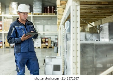 A Worker In Overalls And A Helmet In A Warehouse Inspects Products Stored In Barrels. Calculation And Verification Of Reserves In An Oil Company, Solving Logistics Problems