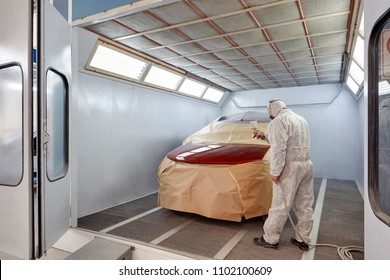 Worker painting a car in garage using an airbrush gun