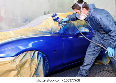 Worker painting a car in a paint booth,