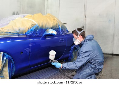 Worker painting a car in paint booth.
