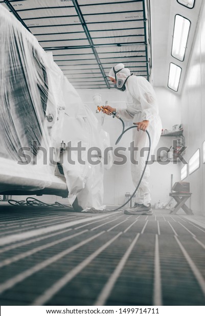 Worker\
painting car in a paint booth, low angle\
image.