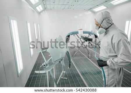 Worker painting a car parts in a paint booth,