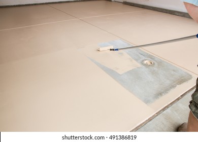 Worker Painting Floor Of Garage With Roller.