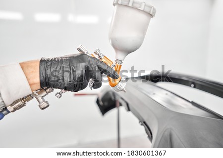 Worker painting parts of the car in special painting chamber, wearing costume and protective gear. Car service station.