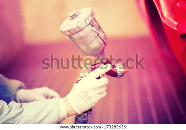 Worker painting a red car in painting booth\
using professional tools and spray\
gun