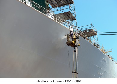 Worker Painting Ship Hull Using Airbrush.