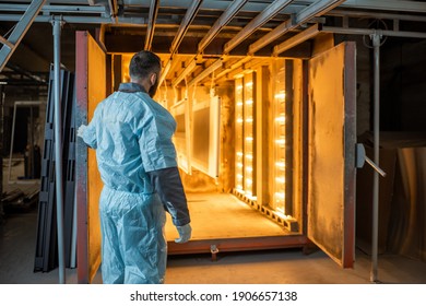 Worker Of The Painting Shop Pushing Metal Products Into The Oven For Baking Powder Paint. Powder Coating Process At The Manufacturing. High Quality Photo