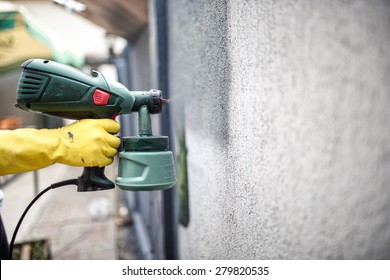 Worker Painting Wall With Grey Paint Using A Professional Spray Gun. Man Painting Wall Using Protective Gloves