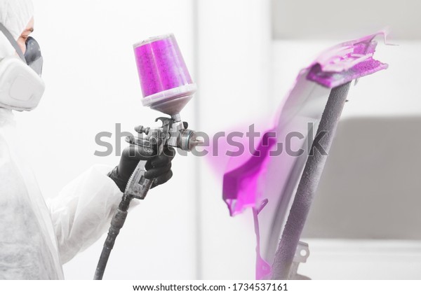 Worker paints element of auto with\
spray gun. White car in a paint chamber during repair\
work.