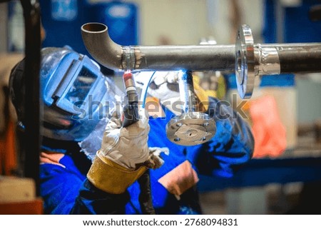Worker performing TIG welding on metal pipeline construction in an industrial plant