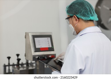 Worker In Personal Protective Equipment Or PPE Inspecting Quality Of Mask And Medical Face Mask Production Line In Factory, Manufacturing Industry And Factory Concept.