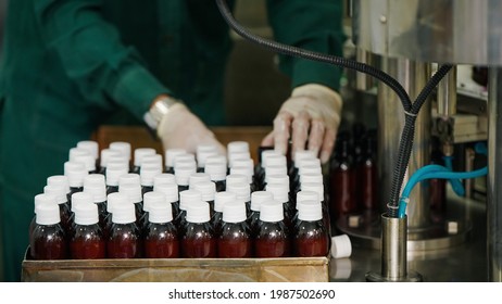 A Worker In A Pharmaceutical Manufacturing Facility Sealing Syrup Bottles Using White Caps.             