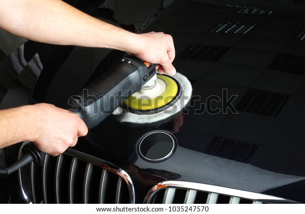 The worker polishes a car cowl with the electric\
tool. Close up.
