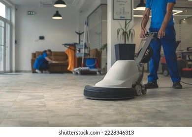 Worker polishing hard floor with high speed polishing machine while other cleaner cleans rhe table in the background - Shutterstock ID 2228346313