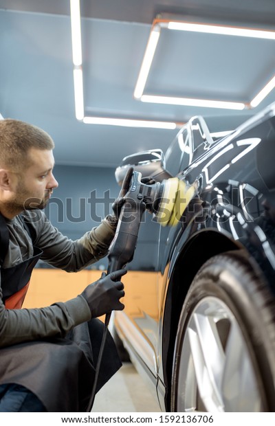 Worker polishing vehicle body with\
special grinder and wax from scratches at the car service station.\
Professional car detailing and maintenance\
concept
