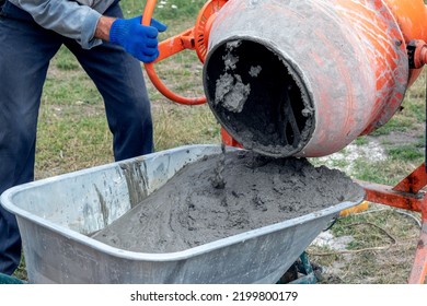 A worker pours cement mortar, concrete, from a concrete mixer into a wheelbarrow. Preparation of cement mortar at the construction site - Shutterstock ID 2199800179