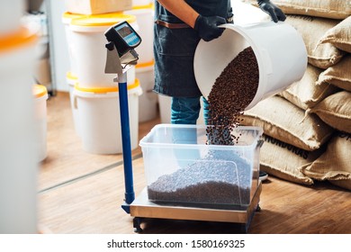 a worker pours roasted coffee beans from a bucket into a tray on a weighing scale, in a warehouse.