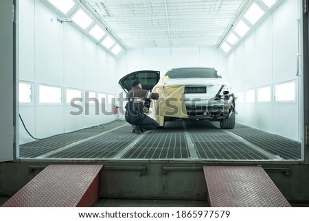 a worker prepares a white car for painting in a car painting booth	