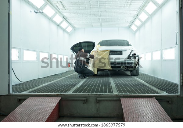a worker prepares a white car for painting in a\
car painting booth	