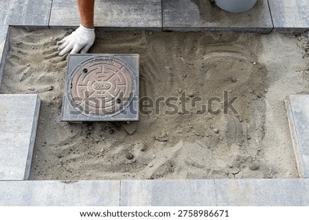 Worker preparing the ground for embedding a cast iron manhole cover in an outdoor paving project
