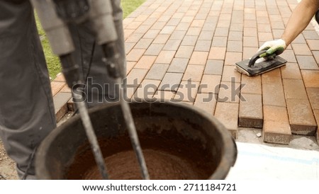 Worker preparing mortar using an electric mixer and spreading grout on freshly laid brick pavers for outdoor flooring