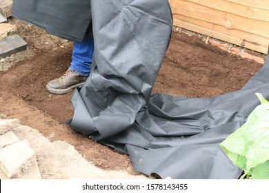 A Worker Preparing A New Garden Pond. Worker Unfolding A Pond Liner In England.