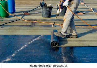 Worker preparing part of bitumen roofing felt roll for melting by gas heater torch flame. On the back of the sheath there is the stamp  "Made in Italy" product - Shutterstock ID 1043528755