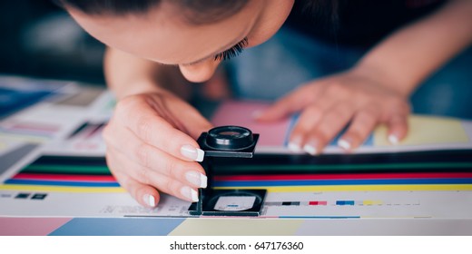 Worker in a printing and press centar uses a magnifying glass and check the print quality