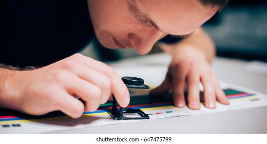 Worker in a printing and press centar uses a magnifying glass and check the print quality - Shutterstock ID 647475799