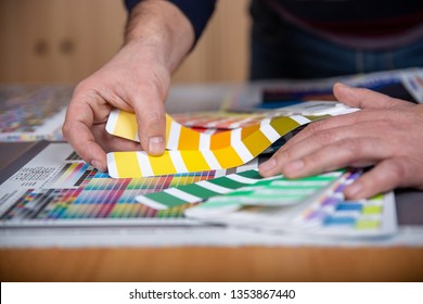 Worker in a printing and press center uses a color palette to select the correct shade of color from CMYK printed sheet.