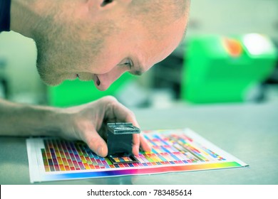 Worker in a printing and press center uses a magnifying glass to check the print quality. Scene showing the print quality control check.
