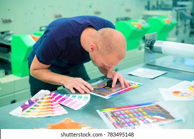 Worker in a printing and press center uses a magnifying glass to check the print quality. Scene showing the print quality control check.